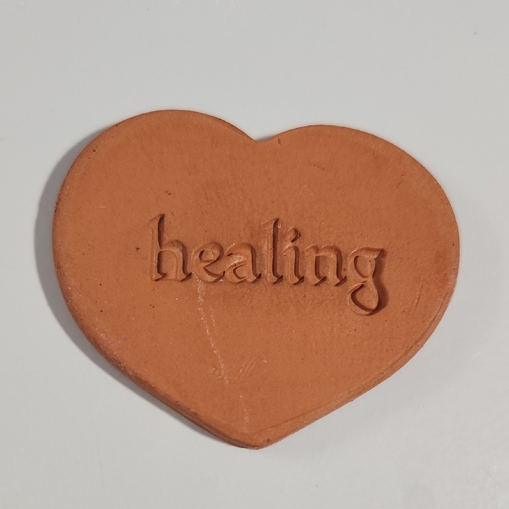 Heart-shaped terracotta disc with the word "healing" impressed on it.